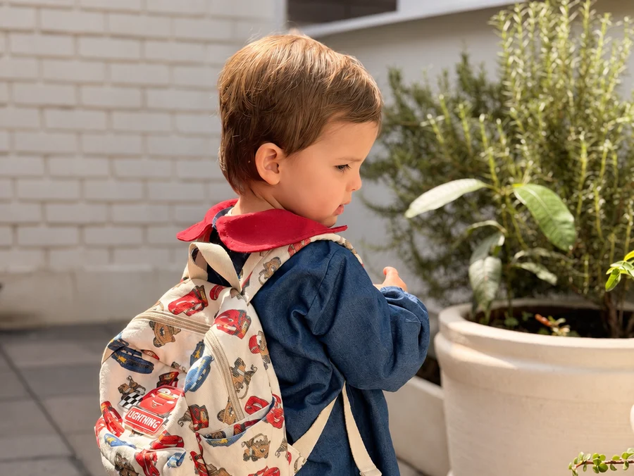 Peque de Pirulí con su uniforme y su mochila de Cars, mirando una planta