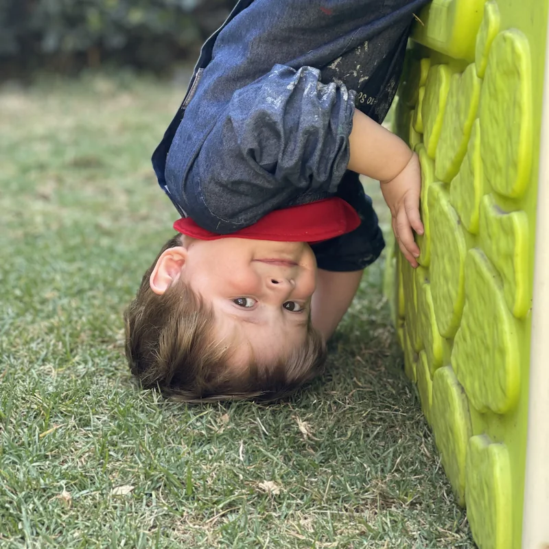 Niño de Piruli de cabeza en los juegos del jardín, sonriendo a la cámara